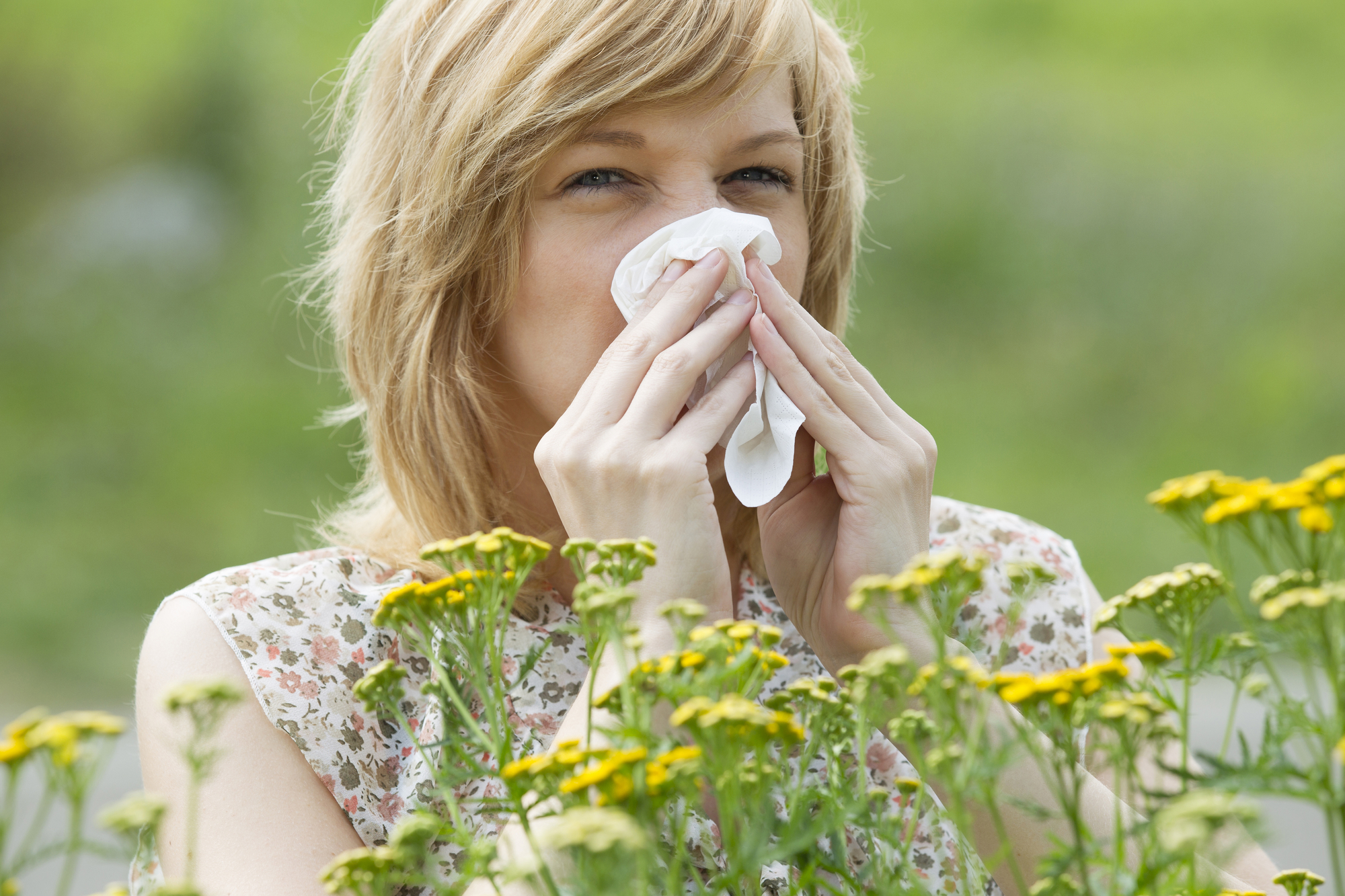 Young woman blowing nose into tissue in front of flowers